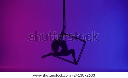 Silhouette of female acrobat isolated on neon background. Woman aerialist dancer spinning in splits in the air on cube with ropes.