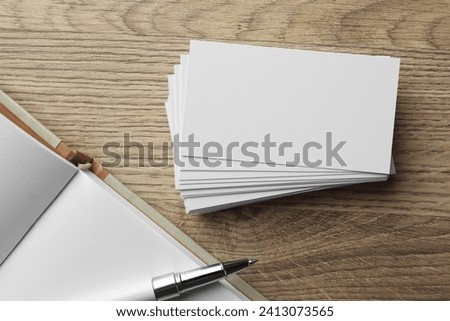 Stack of blank business cards, notebook and pen on wooden table, flat lay. Mockup for design