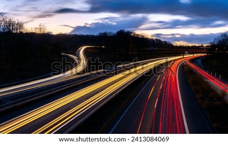 Major autobahn crossing of A40 and A3 in Ruhr Basin Germany near Duisburg, Oberhausen, Essen and Düsseldorf. Panoramic longtime exposure with red and white lights of passing cars at dusk blue hour. Royalty-Free Stock Photo #2413084069