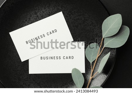 Business cards and eucalyptus branch on black plate, top view