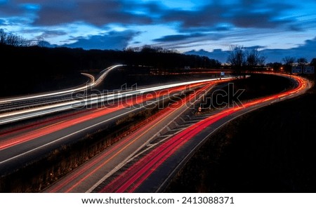 Panoramic longtime exposure of major autobahn crossing of A40 and A3 in Ruhr Basin Germany near Duisburg, Oberhausen, Essen and Düsseldorf.  Red and white lights of passing cars at dusk blue hour. Royalty-Free Stock Photo #2413088371