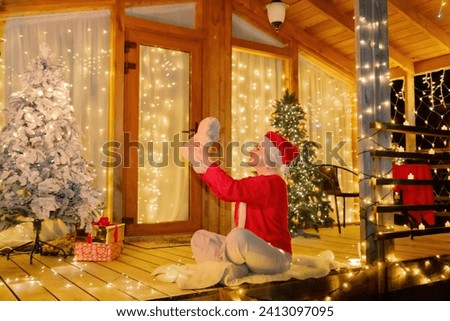 Woman in Santa hat by Christmas tree. Festive setting. Illustrating holiday cheer and celebration. She is posing for a picture, and there are presents nearby, adding to the festive atmosphere.