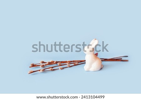 Happy easter decoration with white bunny decorative statuette and willow branch. Minimal isolated festive composition on light pastel blue background. Copy space, place for text, front view