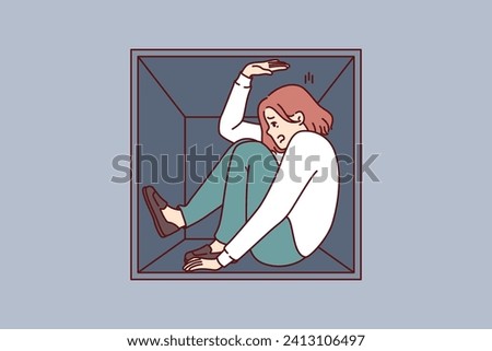 Woman suffering from claustrophobia sits in cramped box and feels pressure of walls, as metaphor for cramped housing. Girl experiences problems due to claustrophobia and fear of closed spaces. Royalty-Free Stock Photo #2413106497