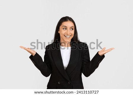 Happy satisfied caucasian businesswoman in suit reacting to great news, raising hands up, rejoicing and smiling, posing on grey studio background