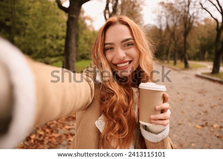 Portrait of happy woman with paper cup taking selfie in autumn park Royalty-Free Stock Photo #2413115101