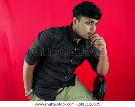 Thoughtful young man posing against a red background with a pensive expression dressed in a checkered shirt