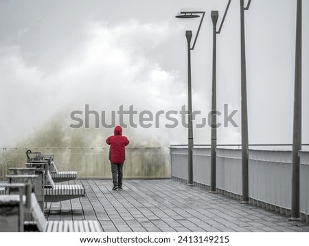 A tourist taking a picture of big crashing wave hitting the pier front