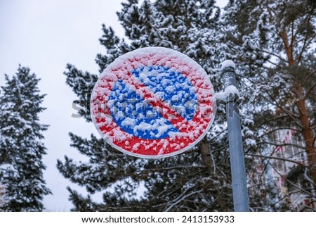 A road sign prohibiting parking is covered with sticky snow. "No Parking" sign under the snow shot close-up.
