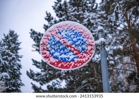 A road sign prohibiting parking is covered with sticky snow. "No Parking" sign under the snow shot close-up.