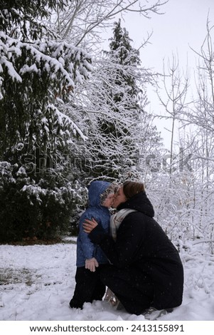 Mom with daughter in winter snowy forest. Mom kisses her daughter and warms her hands with her breath. Young girl with her daughter walking in the forest in winter.