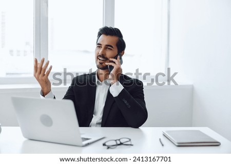 Man in office businessman sitting at desk and working in laptop and talking on phone, modern suit, finance and startup concept and data analysis, working lifestyle in bright office.