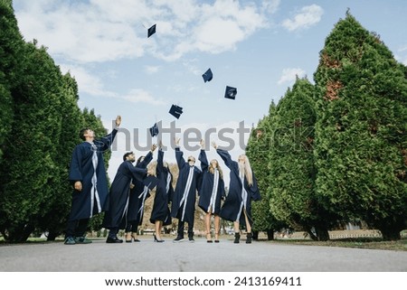 Friends in graduation uniform celebrate the joy of graduating by throwing caps and creating beautiful memories together in a park outdoors. Royalty-Free Stock Photo #2413169411