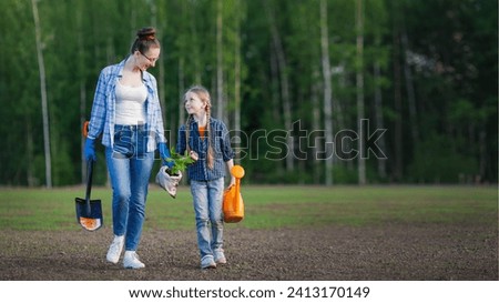 Mother and her little daughter walks together. They are going to plant small tree seedling on the lawn of fresh grass. Ecology education, growing of nature lover. 16:9 wide image. Royalty-Free Stock Photo #2413170149