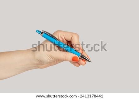 Closeup of woman hand holding blue ballpen writing empty space for advertisement. Indoor studio shot isolated on gray background. Royalty-Free Stock Photo #2413178441