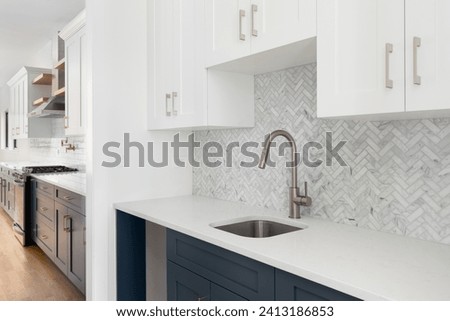 A scullery or butler's pantry detail with a bronze faucet and hardware, blue and white cabinets, and marble herringbone tile backsplash and countertop. Royalty-Free Stock Photo #2413186853