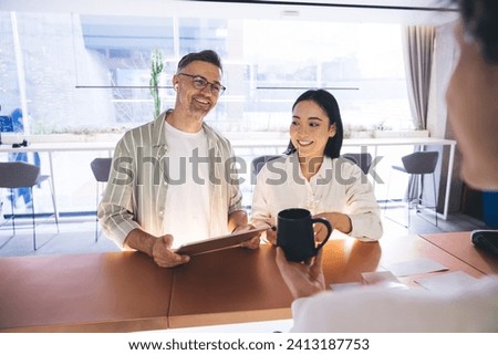 Happy male and female colleagues communicate with receptionist in corporate company, cheerful employees with touch pad technology talking with administrator about organization of business events Royalty-Free Stock Photo #2413187753