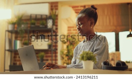 African american woman works at home during sunset hour, publishing blog article on personal website. Freelancer seeking to build online e business while refining abilities. Handheld shot. Royalty-Free Stock Photo #2413196211