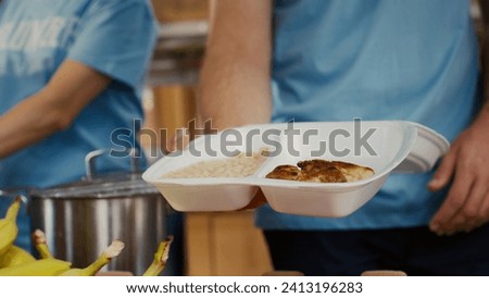 Close-up on caucasian man serving bread chicken and baked beans to poor hungry person at food drive. Detailed view of meal box from hunger relief team given to the needy. Selective-focus handheld. Royalty-Free Stock Photo #2413196283