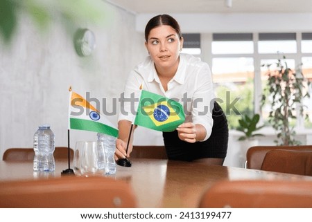 Young woman setting up flags on table for international negotiations between india and brazil