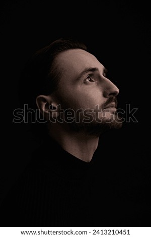 Portrait in profile of a dark-haired man who looks up, thoughtful. Art photography in a dark key. Black background with copy space.