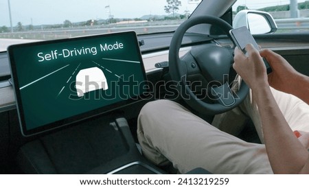 Self driving car or autonomous vehicle travel on speed highway with driverless system and autopilot mode allowing man driver relax and focus on smartphone without compromising safety. Perpetual Royalty-Free Stock Photo #2413219259