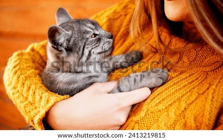 The image depicts a woman holding a small to medium-sized domestic cat. The cat has fur and whiskers, and the interaction appears to be taking place indoors.