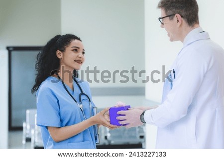 Smart male doctor is giving a surprise birthday or special gift or present to a female nurse in a hospital ward, concept of coworker excitement, positive, colleague relationship, friendship thank you.