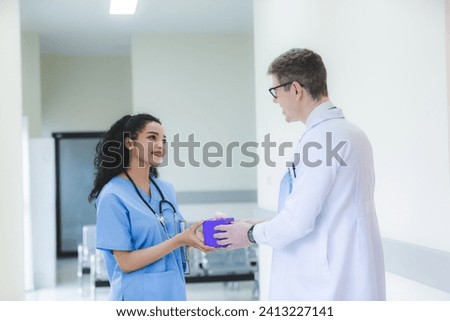 Smart male doctor is giving a surprise birthday or special gift or present to a female nurse in a hospital ward, concept of coworker excitement, positive, colleague relationship, friendship thank you.