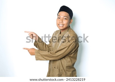 asian muslim man pointing to the right side and smiling at camera wearing islamic dress isolated on white background