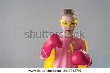 Child in boxing gloves with a yellow ribbon as a symbol of the fight against cancer. Increasing the level of knowledge about kids who have overcome tumor diseases.