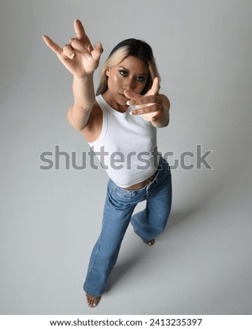 Full length portrait of brunette female asian model wearing casual clothes, white singlet shirt, denim jean pants. Standing pose, high camera angle for perspective. isolated on white studio background