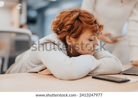 A tired businesswoman sleeping at her desk in the office, taking a moment to relax during her busy workday.