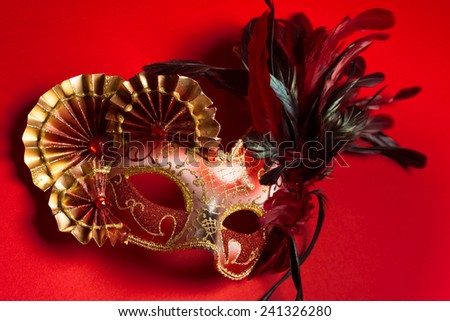 A red and gold venetian, mardi gras mask on a red background