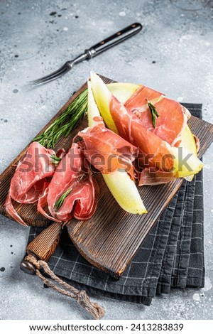 Spanish Tapas Jamon Iberico with goat cheese, melon and honey on a wooden board. Gray background. Top view. Royalty-Free Stock Photo #2413283839