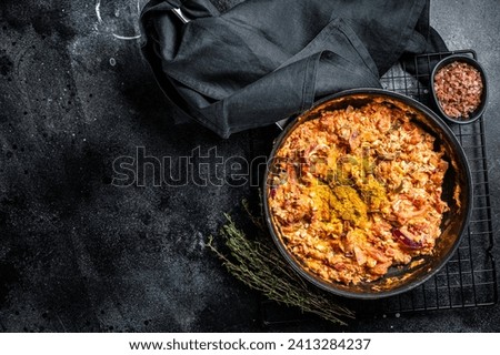Turkish Menemen omelet in a frying pan. Black background. Top view. Copy space. Royalty-Free Stock Photo #2413284237