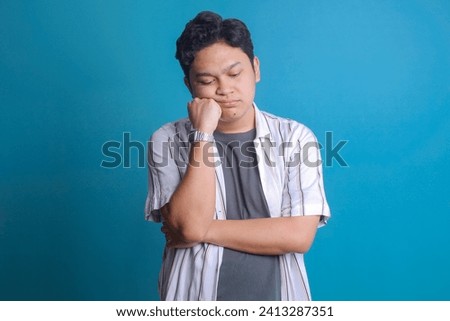 Young Asian man looking sleepy and bored over blue background