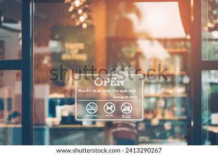 Stickers showing opening and closing times. An open sign on the front window of a coffee shop or cafe and a blurred, bokeh image inside the shop.