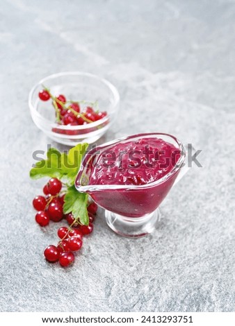 Red currant sauce in a glass sauceboat, berries in a bowl and on the table against the background of a granite table Royalty-Free Stock Photo #2413293751