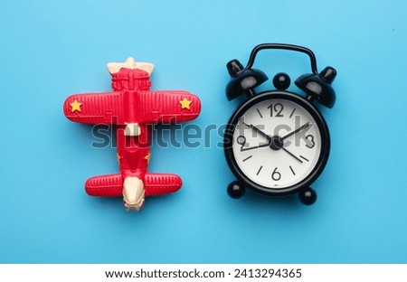 A flatlay picture of toy aeroplane and alarm clock on blue background. Flight time concept.