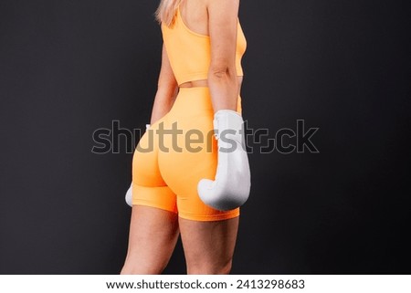 Woman boxer in gloves training on yellow and dark studio background