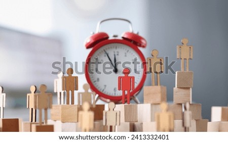 Wooden figurines with one red figure stand next to alarm clock. Time management and individual approach business planning concept Royalty-Free Stock Photo #2413332401