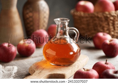 A glass jug of apple cider vinegar with fresh fruit on a table Royalty-Free Stock Photo #2413337037