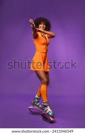 Sporty curly woman in orange outfit posing in kangaroo jumpers on studio background