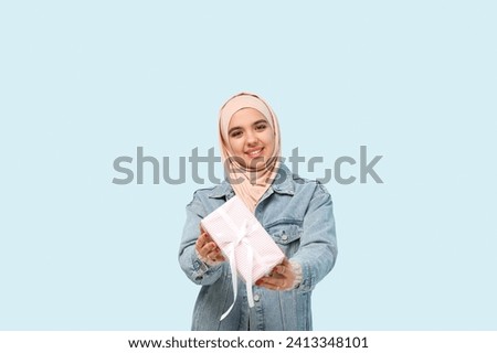 Happy young Muslim woman in hijab with gift box on blue background