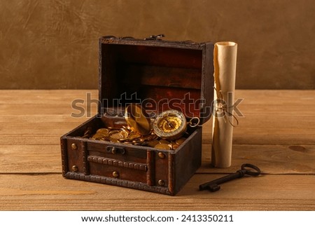 Old chest with coins, compass and map on wooden table near brown wall