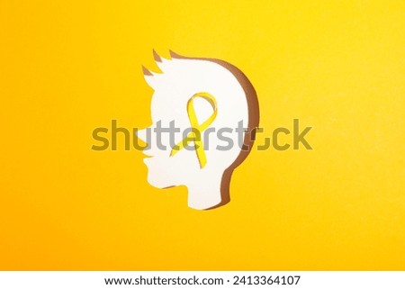 A child's head made of white paper with a yellow ribbon