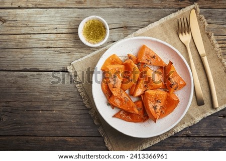 roasted pumpkin, pieces in plate with oil, thyme, a honey and seasonings, old rustic wooden dark table, copy space