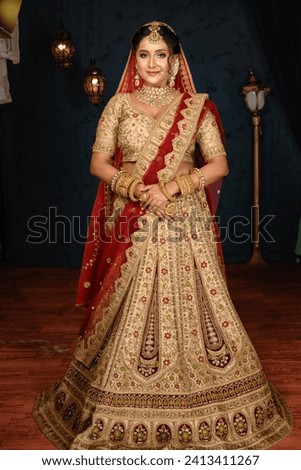 Stunning Indian bride dressed in traditional bridal lehenga with heavy gold jewellery and veil posing fashionable in studio lighting. Wedding fashion and lifestyle. Royalty-Free Stock Photo #2413411267