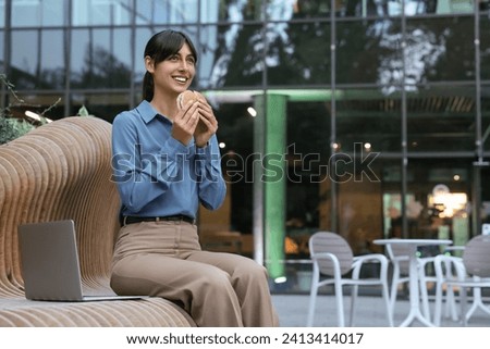 Lunch time. Happy businesswoman with hamburger on bench outdoors